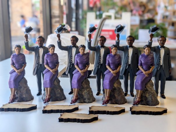 Figures of six people in formal attire, with two holding hats, seated on pedestals.